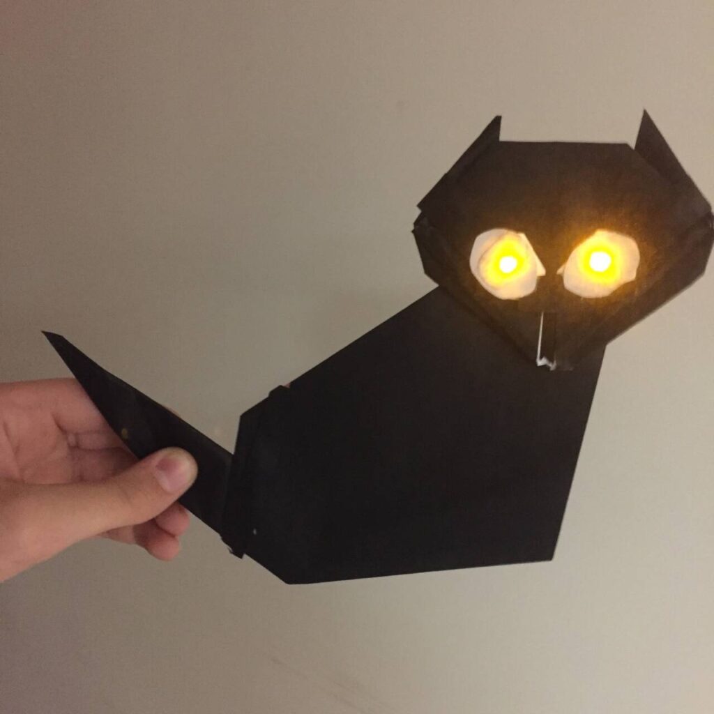 a folded paper black cat with illuminated LED eyes