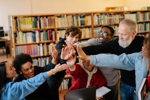 Diverse group of students and a teacher high-fiving in a library. Celebrating teamwork and education.