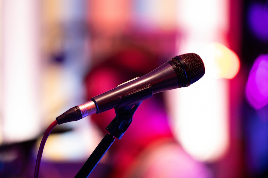 Close-up shot of a microphone on stage with colorful background bokeh, capturing live performance ambiance.