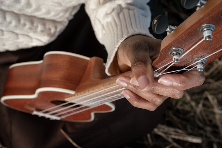Detailed view of a person playing a wooden ukulele, showcasing strings and hand positioning.