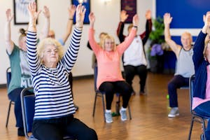 Group of senior adults participating in a chair exercise class, promoting fitness and healthy lifestyle.