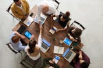Top view of a diverse team collaborating in an office setting with laptops and tablets, promoting cooperation.