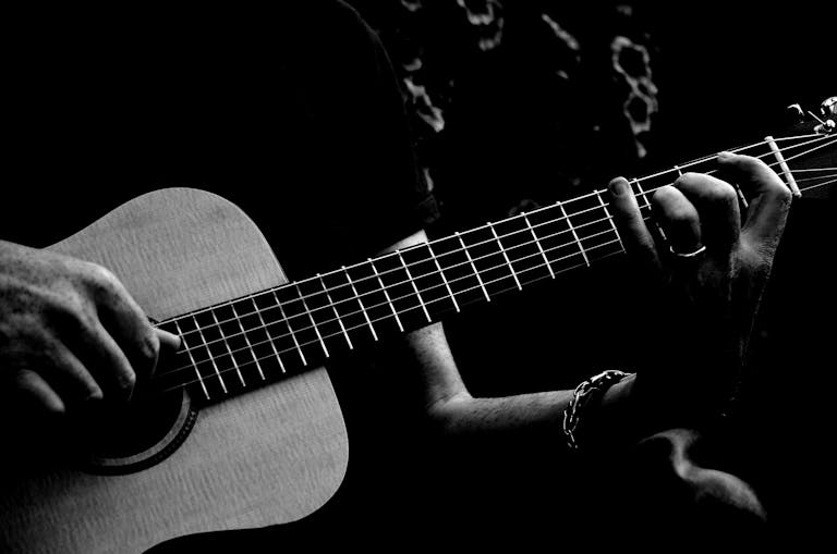 Black and white image of a person strumming an acoustic guitar, focusing on hands.