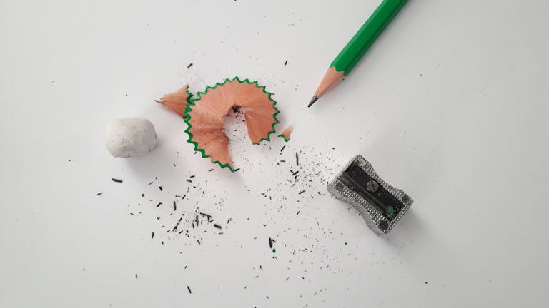 Close-up of pencil, sharpener, and eraser on a clean white surface, capturing a moment of creativity.