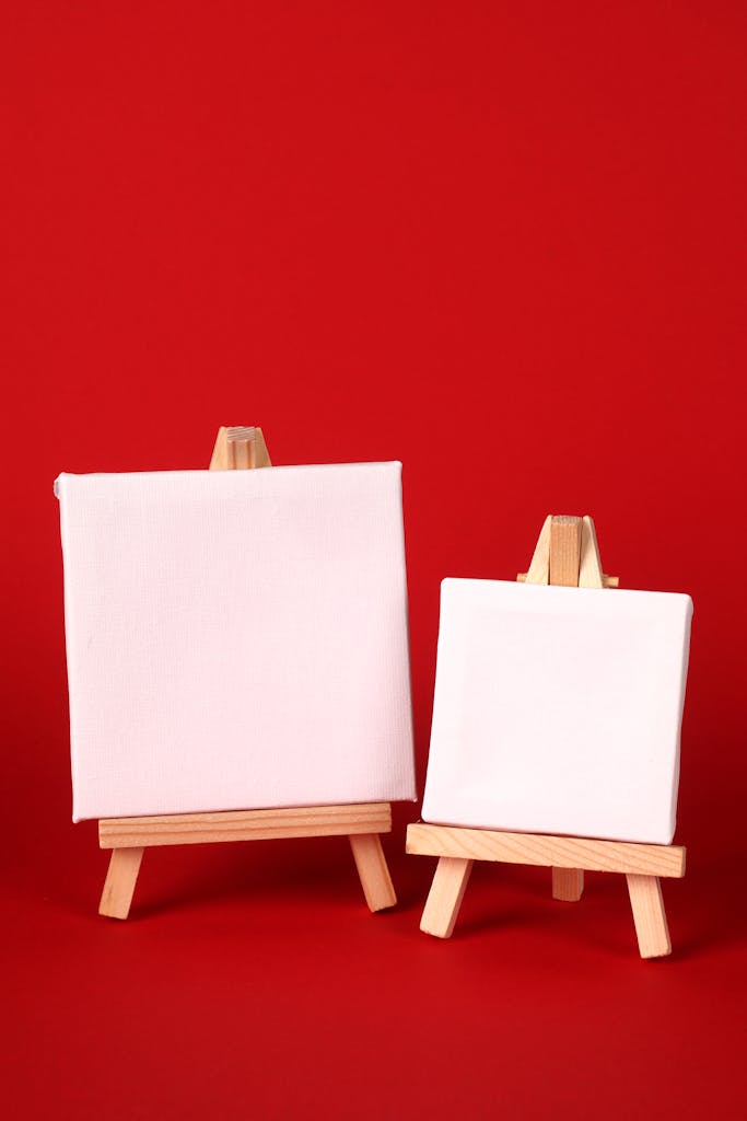 Pair of white canvases on wooden easels over red background, ideal for art presentation.