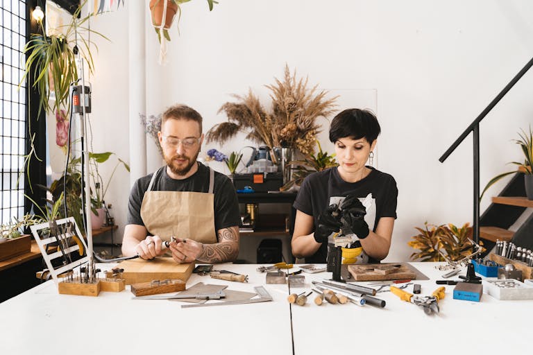 Two artisans creating jewelry with precision and creativity in a modern, plant-adorned studio.