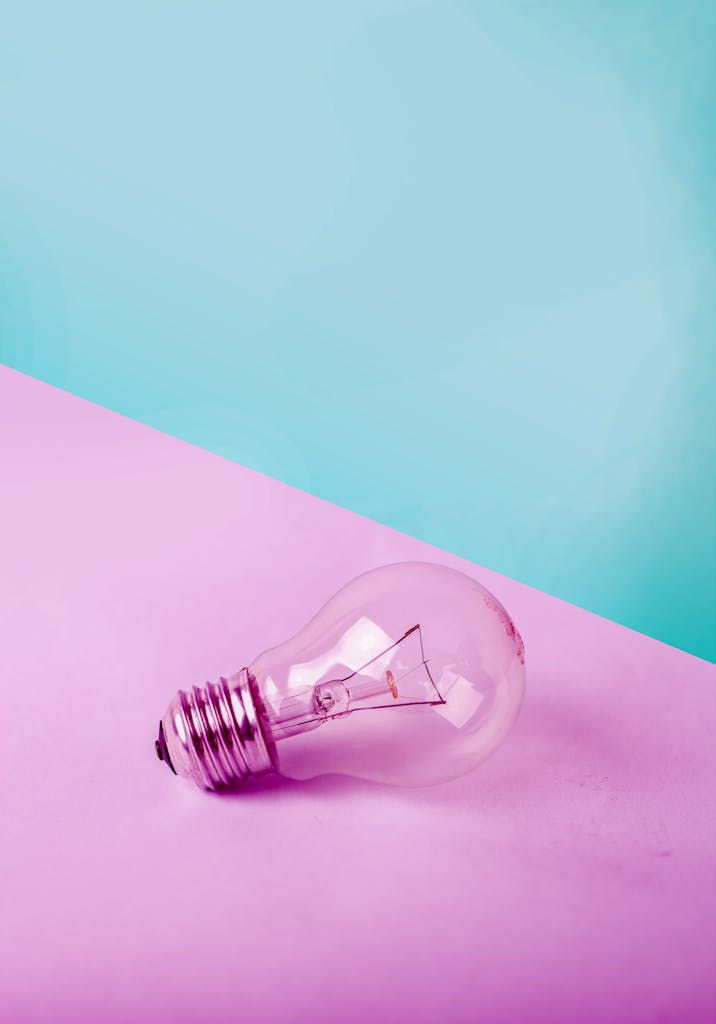 A clear lightbulb on a pastel pink and blue background, symbolizing creativity and ideas.