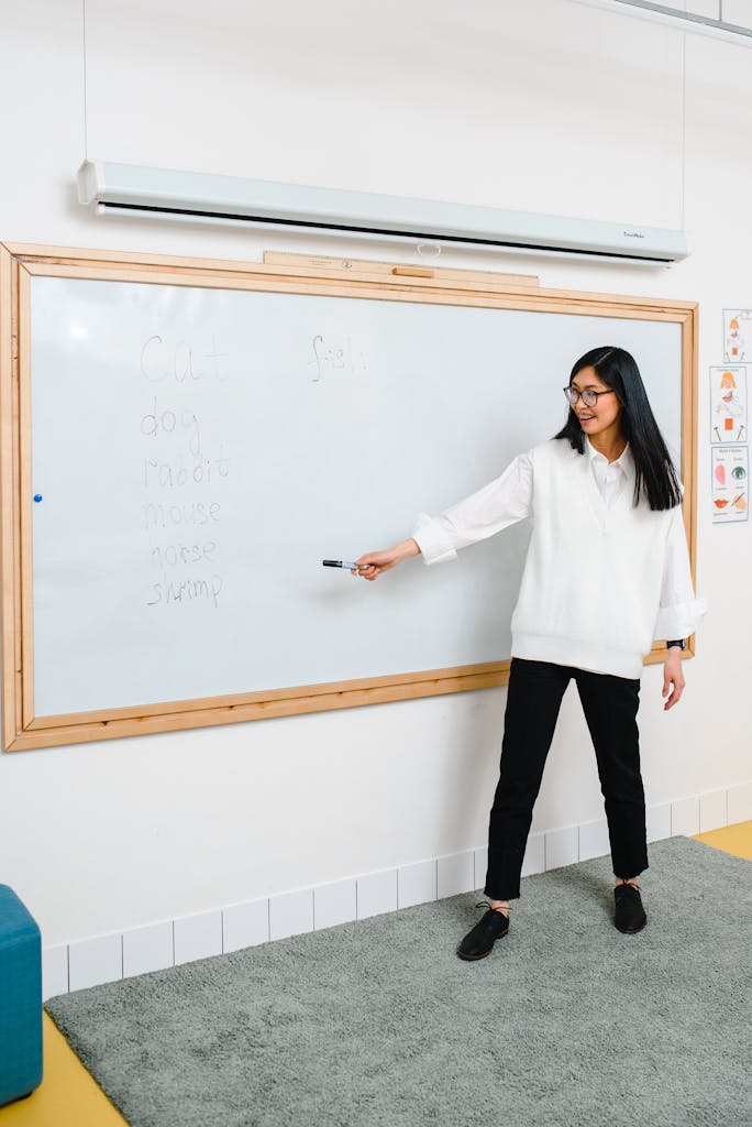 Female teacher explaining lesson on a whiteboard in a classroom setting.
