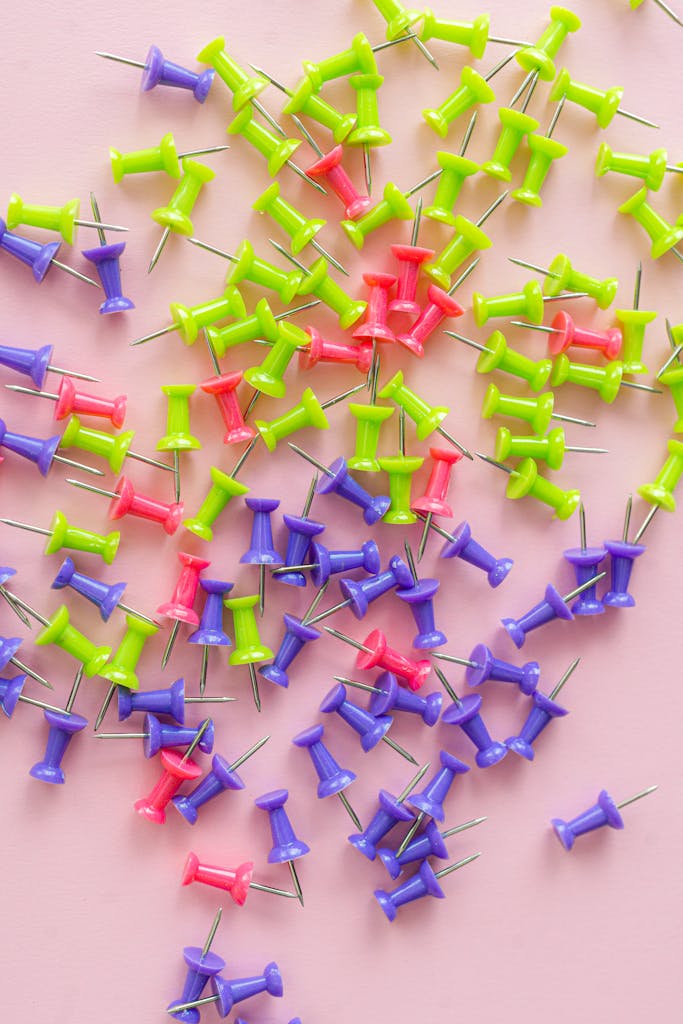 Vibrant colored thumb tacks scattered on a pink surface, top-down view.