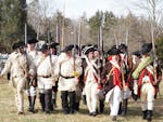 Revolutionary War reenactors in period uniforms march together outdoors in Washington Crossing, PA.