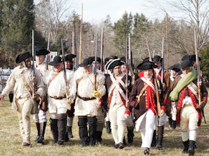 Revolutionary War reenactors in period uniforms march together outdoors in Washington Crossing, PA.