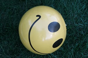 Close-up of a yellow smiley face ball resting on green grass.