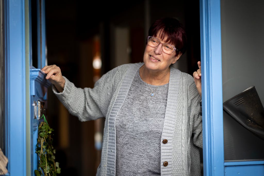Senior woman standing in a doorway, smiling warmly, wearing a cardigan.