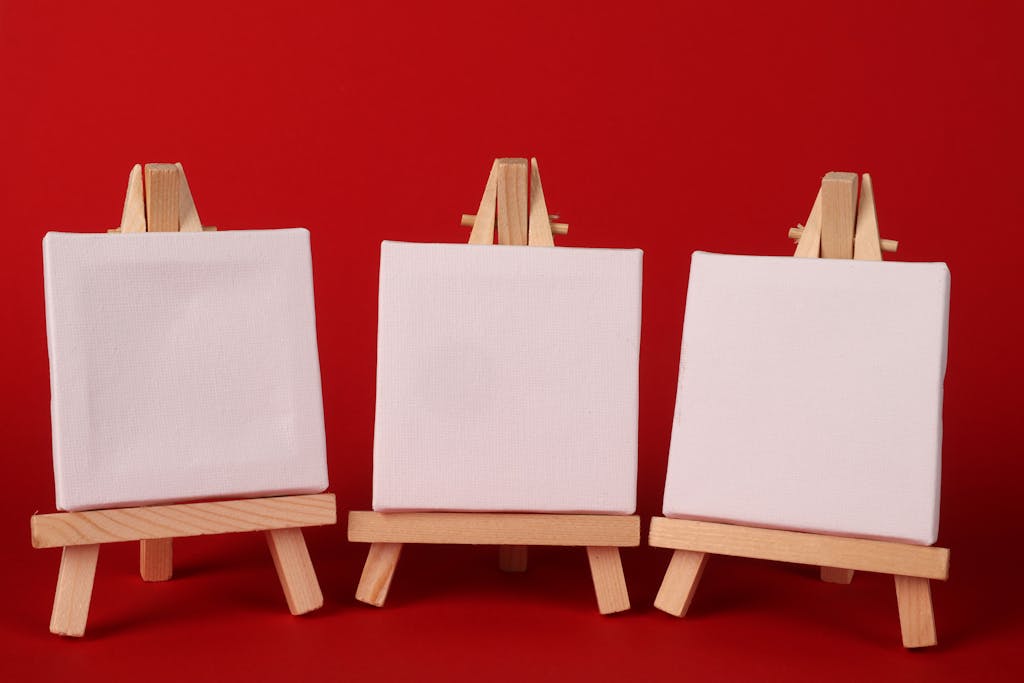 Three blank canvases on wooden easels against a vivid red backdrop, perfect for creative projects.