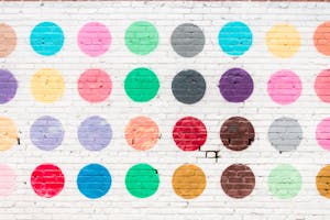 Vibrant polka dot pattern mural on a textured white brick wall.