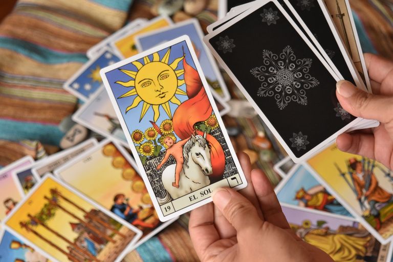 Close-up of tarot cards in hands, showcasing 'El Sol' card. Ideal for fortune-telling and spirituality themes.