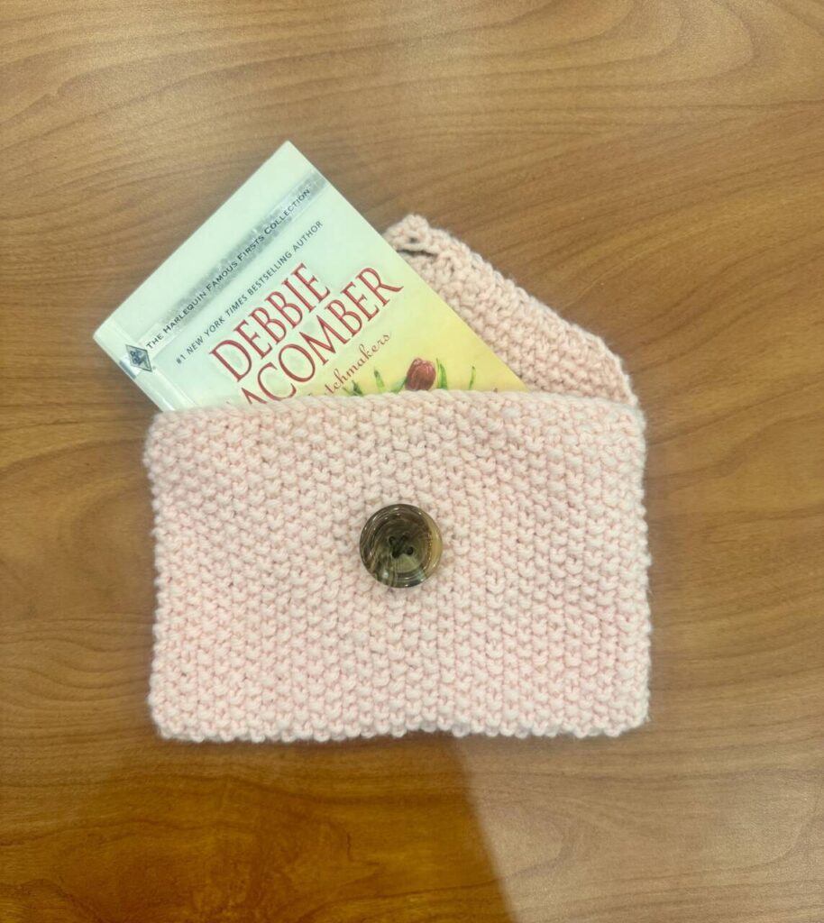 Knitted pouch with button holding a paperback book