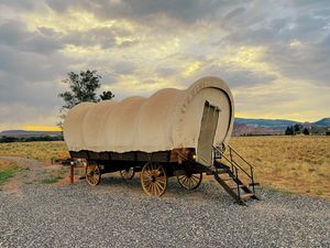 A classic covered wagon sits in a scenic field under a dramatic sunset sky in Utah.