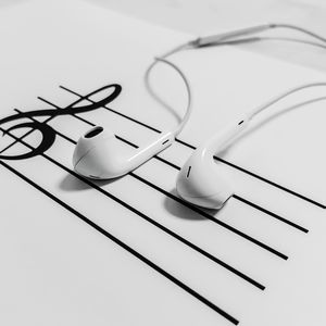 High-angle view of white earphones placed on a music sheet with notes, emphasizing modern audio technology.