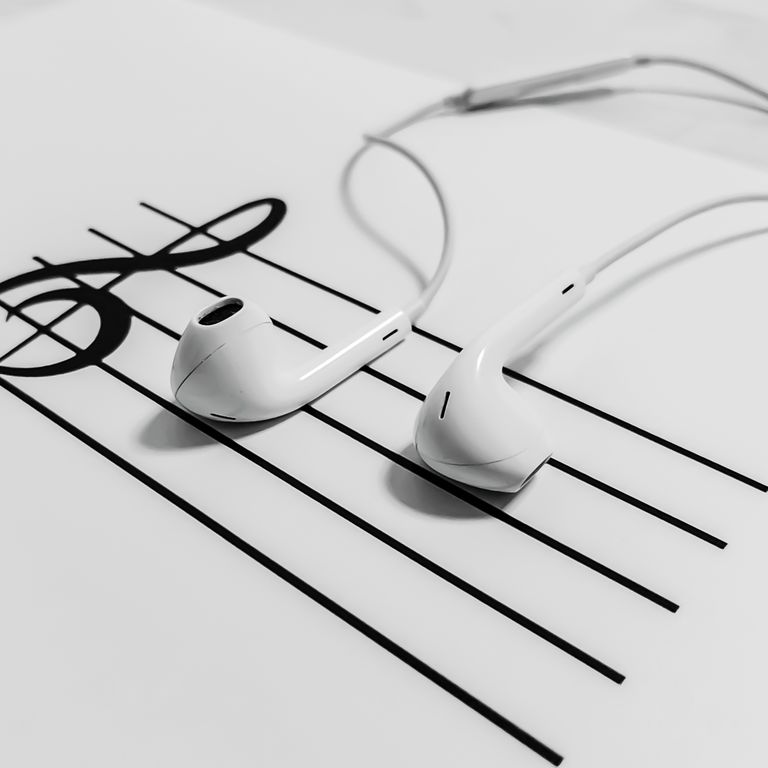 High-angle view of white earphones placed on a music sheet with notes, emphasizing modern audio technology.