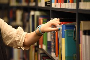 Close-up of a hand selecting a book from a library shelf, showcasing a casual bracelet.